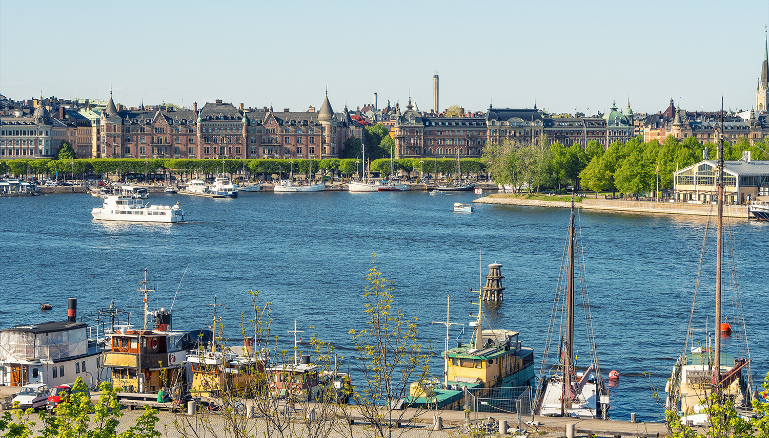 Strandpromenad med båtar och byggnader vid vattnet i Stockholm.